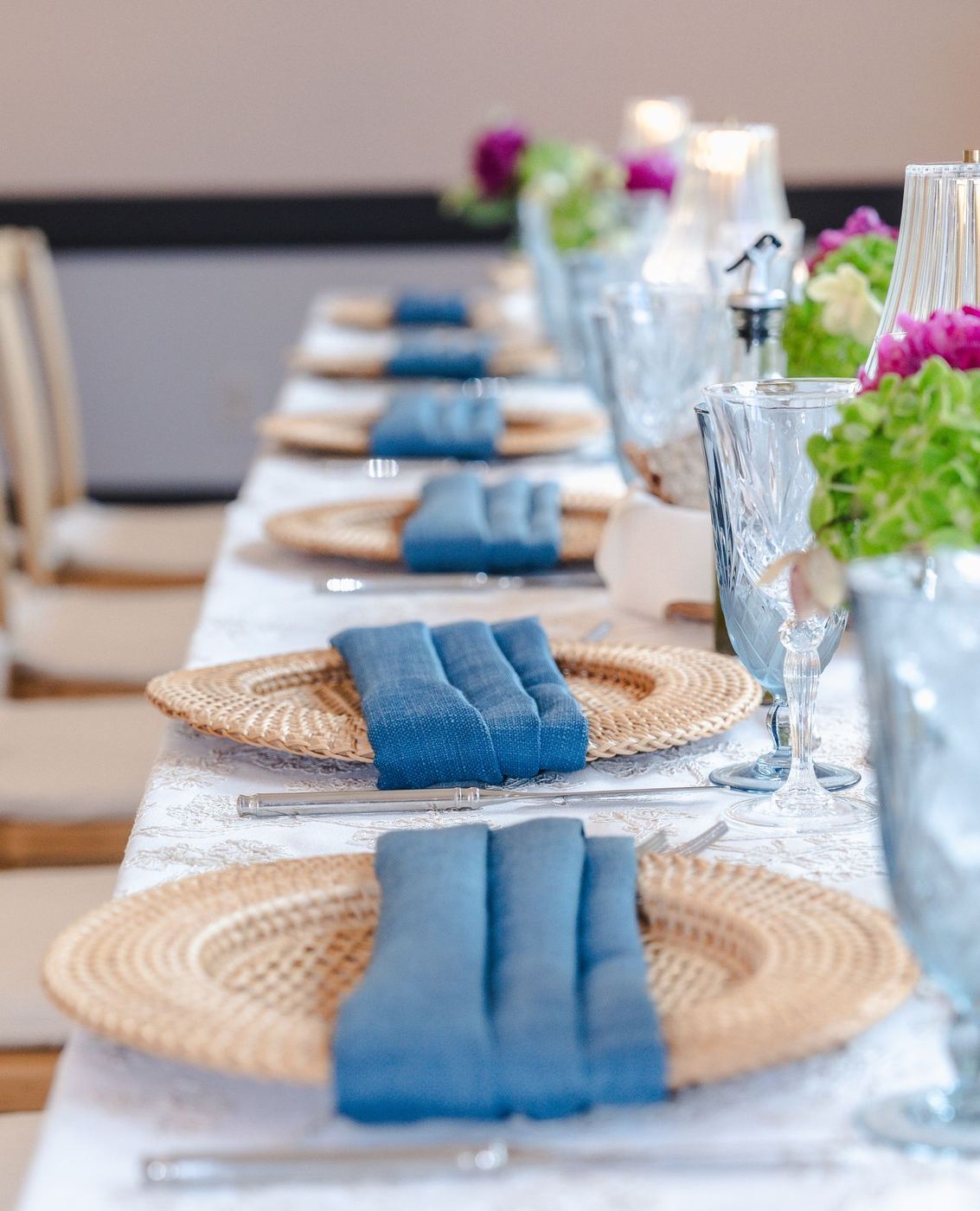 A row of Honey Rattan chargers down a long table, each with a midnight blue Expo napkin