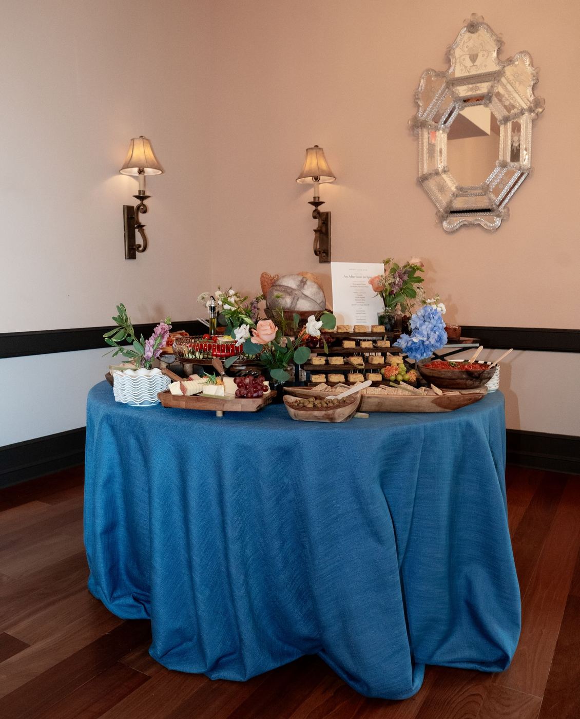 Round grazing table in a floor-length midnight blue Expo cloth, set with breads, cheeses and blue hydrangeas